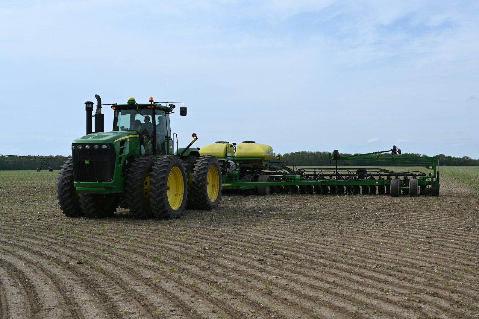 Green tractor planting across a lush farm field